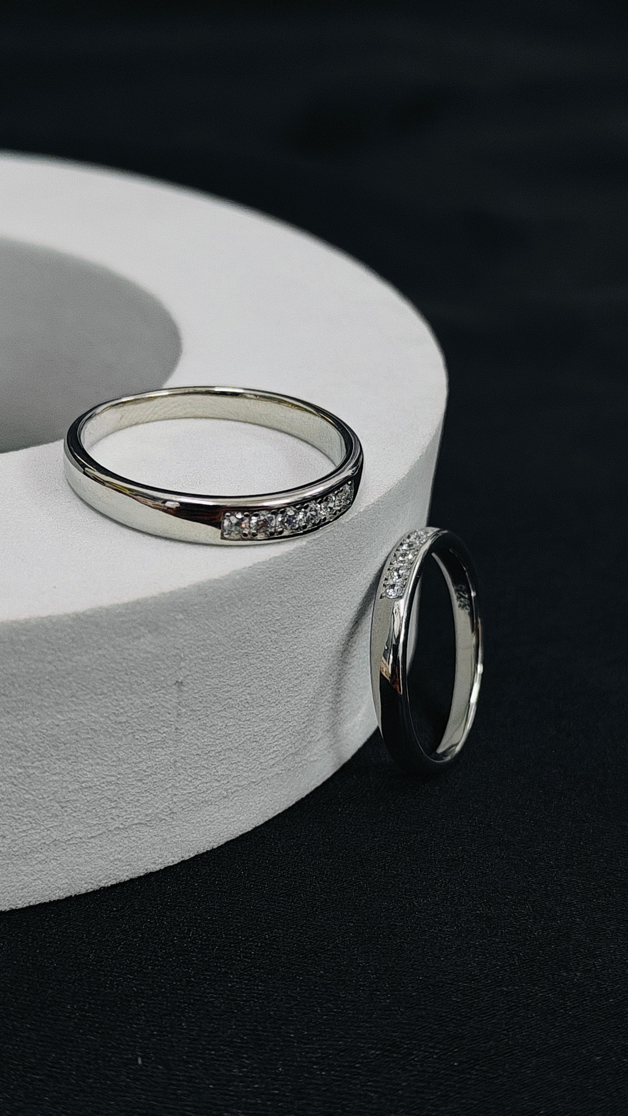 Two silver rings with gemstones on a white circular stand against a dark background